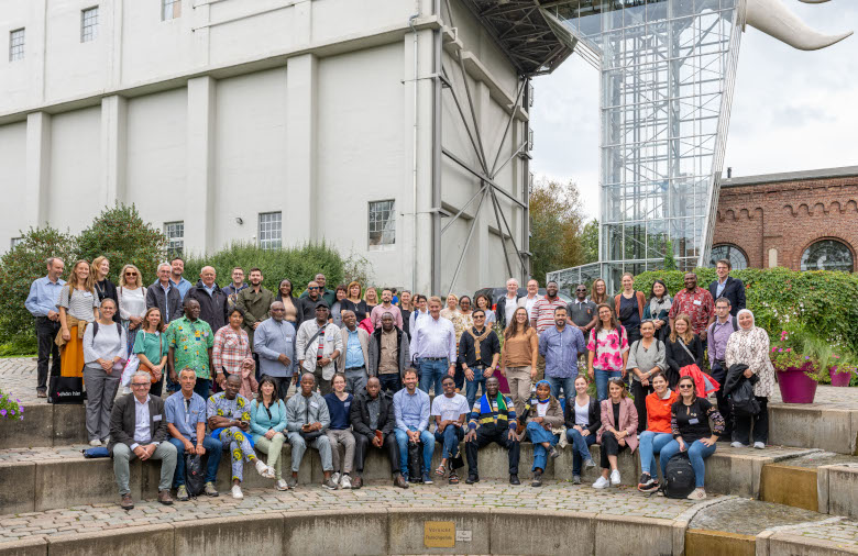 Participants at the inaugural conference in front of an industrial building with a glass lift in the shape of an elephant's trunk.